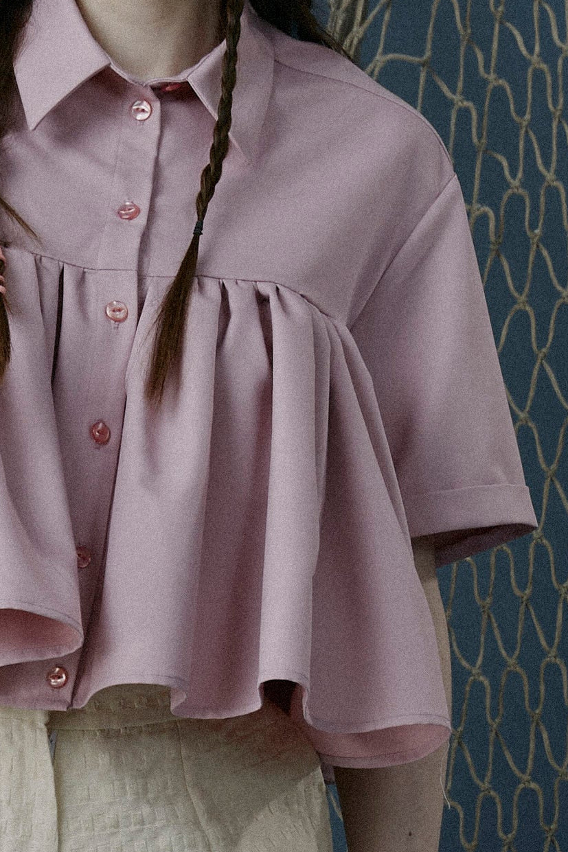 Woman in a pink blouse and beige shorts standing in front of fishing nets.