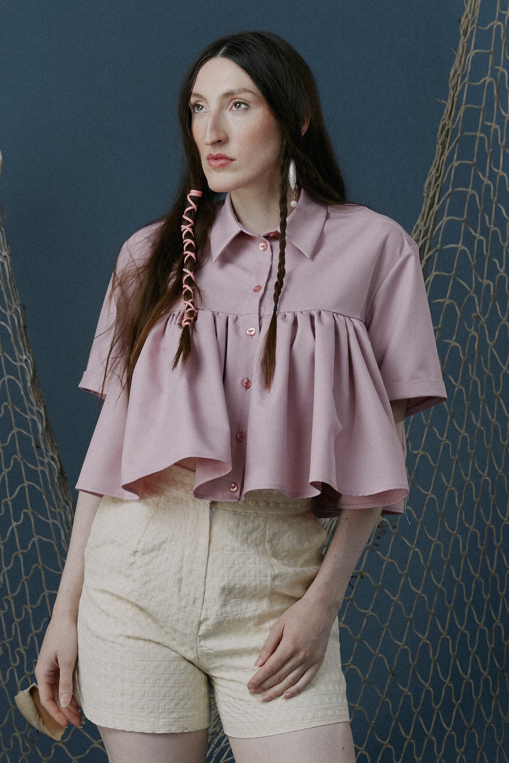 Woman in a pink blouse and beige shorts standing in front of fishing nets.